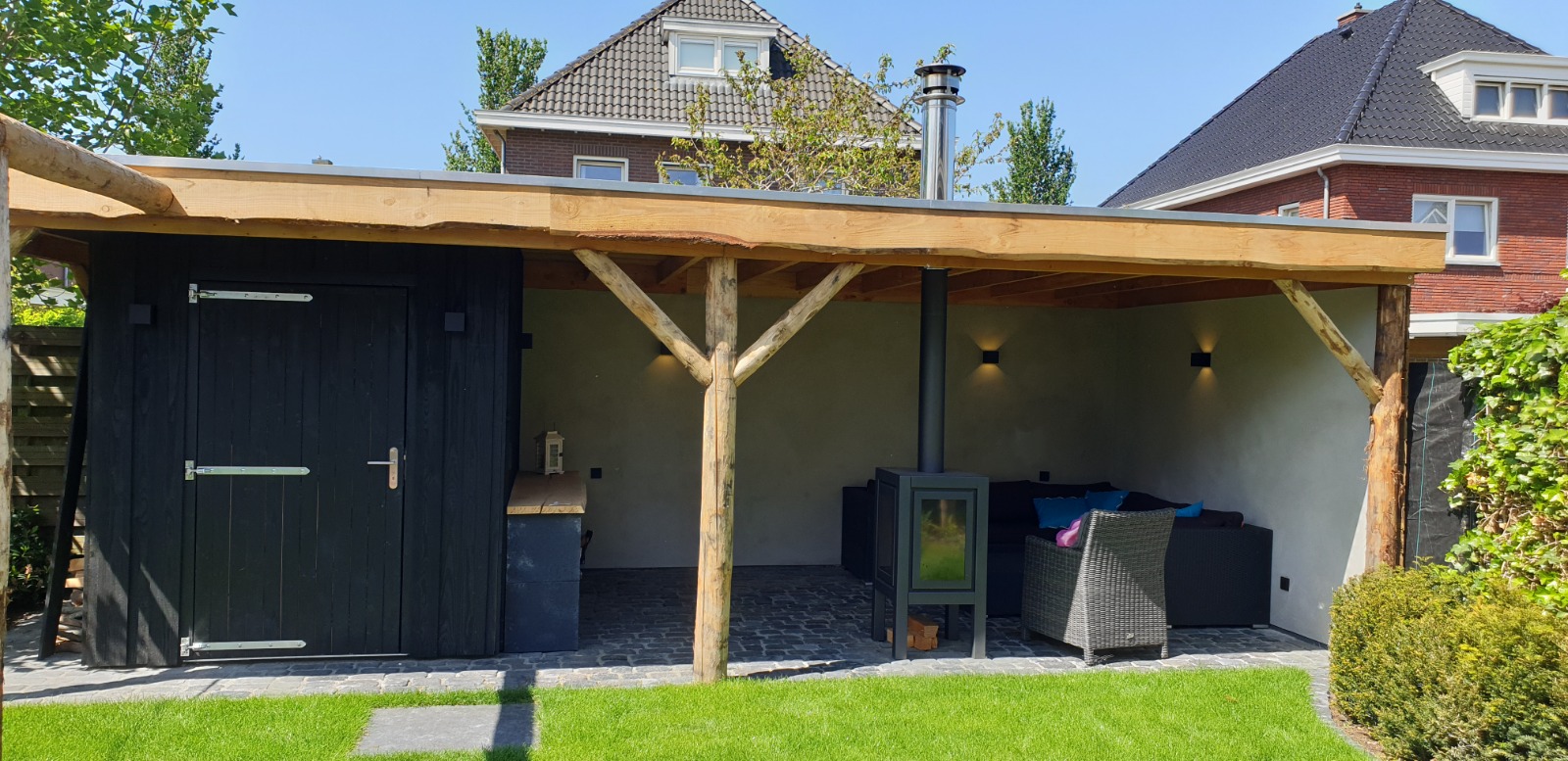 Houten overkapping met berging, loungehoek en houtkachel in de tuin